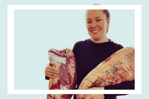 A woman proudly holding two heavy briskets, representing the weight she lost through her macro journey.